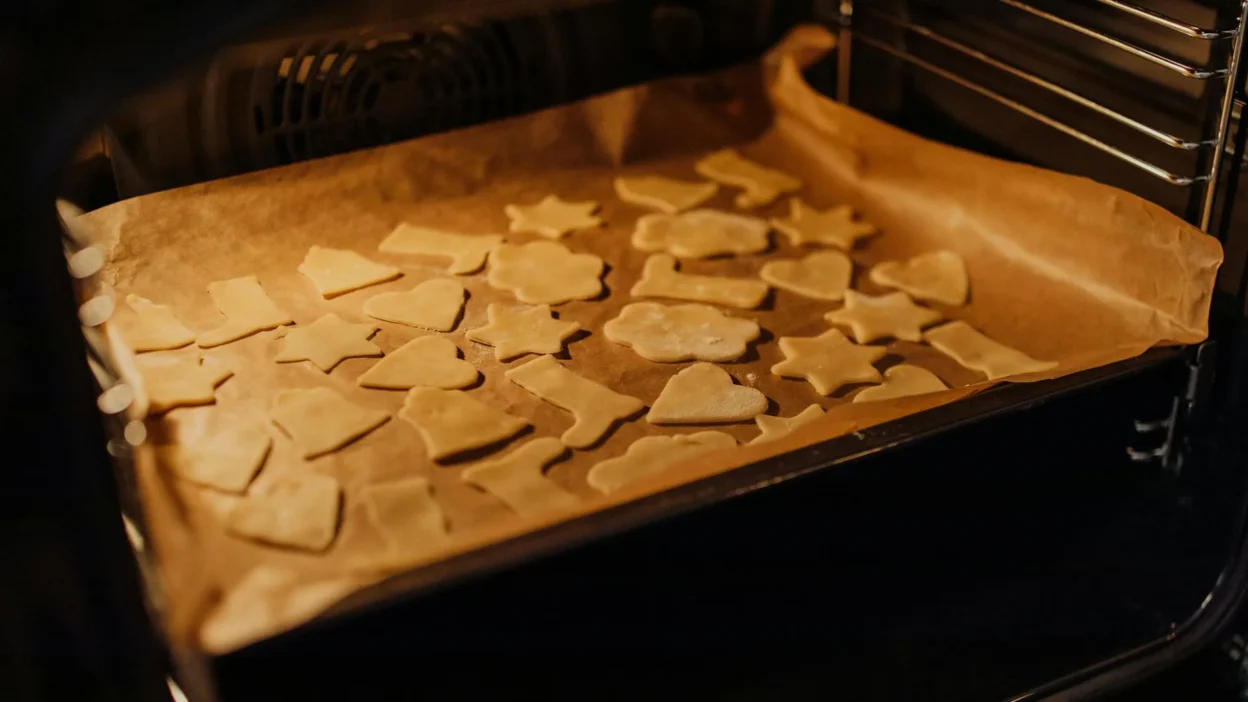 A toaster oven and a full-size oven side-by-side with a small baking sheet of cookies inside the toaster oven.