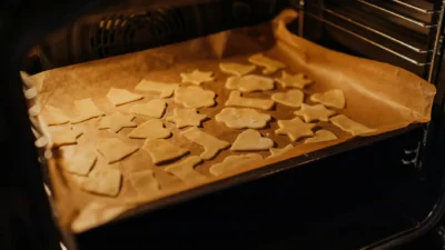 A toaster oven and a full-size oven side-by-side with a small baking sheet of cookies inside the toaster oven.